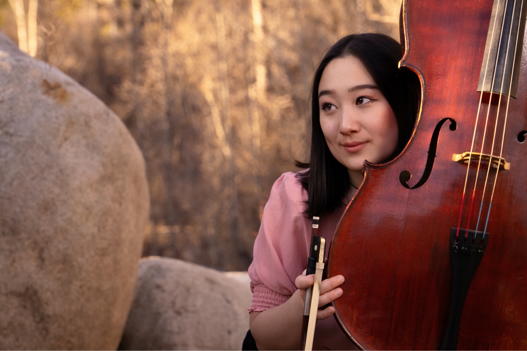 Erica, gently holding her cello by a pile of large boulders